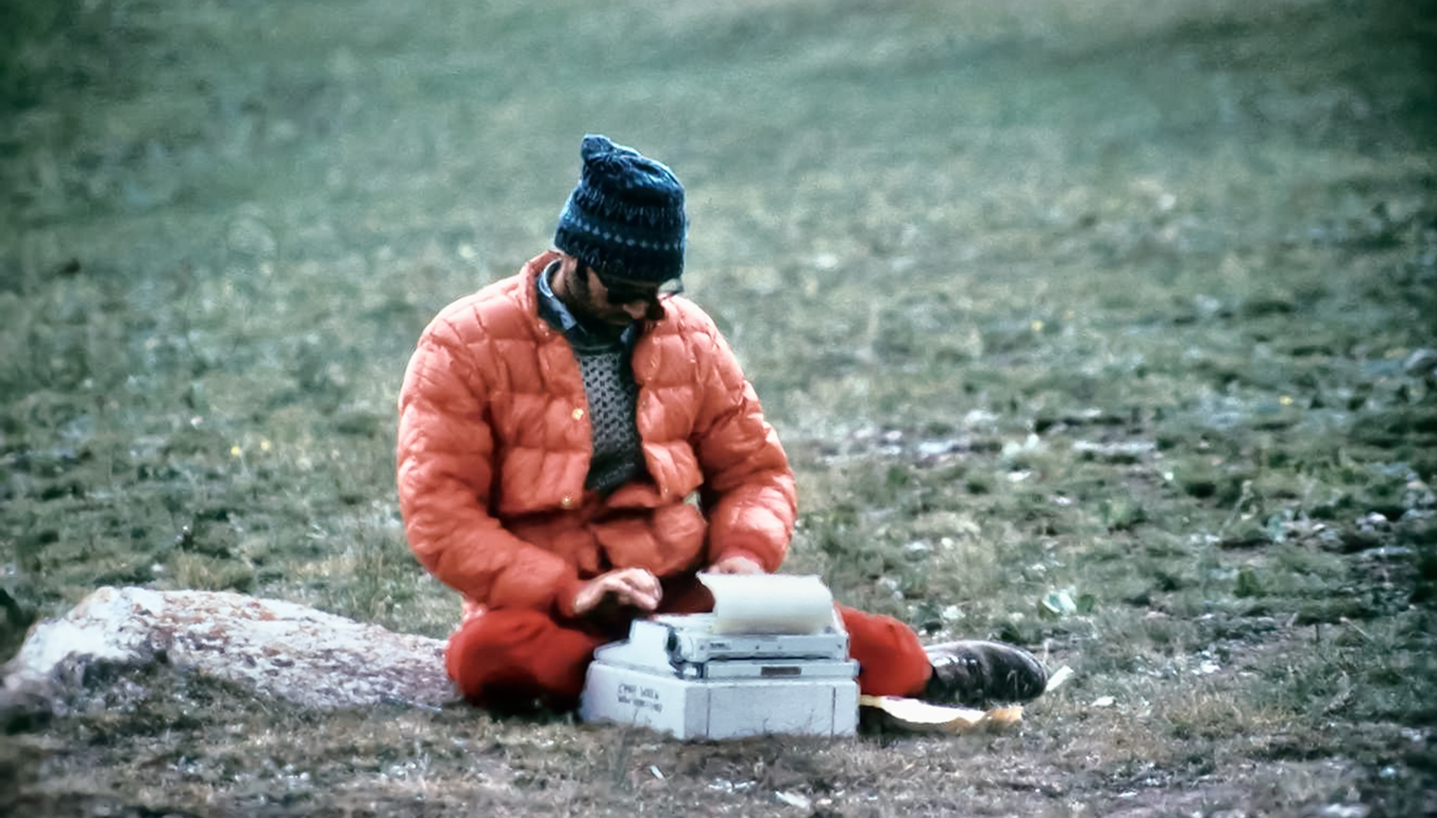 Man in field typing on typewriter