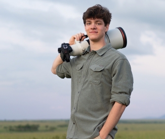 Man standing in field, holding large camera over shoulder