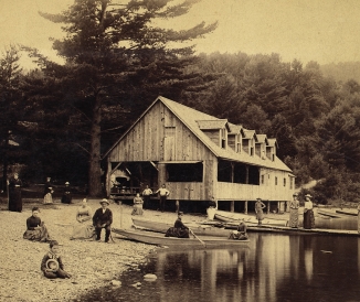 Historic, sepia-toned photo of people at the water's edge at a camp, some in boats