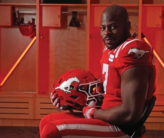 Football player sitting in locker room, holding helmet
