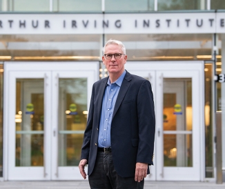 Man wearing suit, standing in front to building that says Arthur Irving Institute