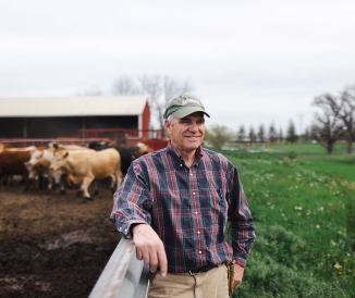Man wearing flannel, standing next to pen with cows