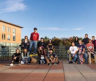 Two groups of students posing with skateboards and helmets on campus