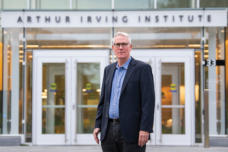 Man wearing suit, standing in front to building that says Arthur Irving Institute