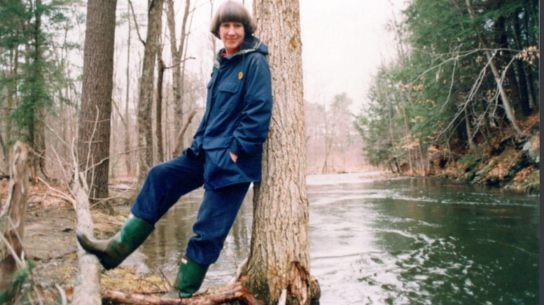 Woman leaning against tree next to water