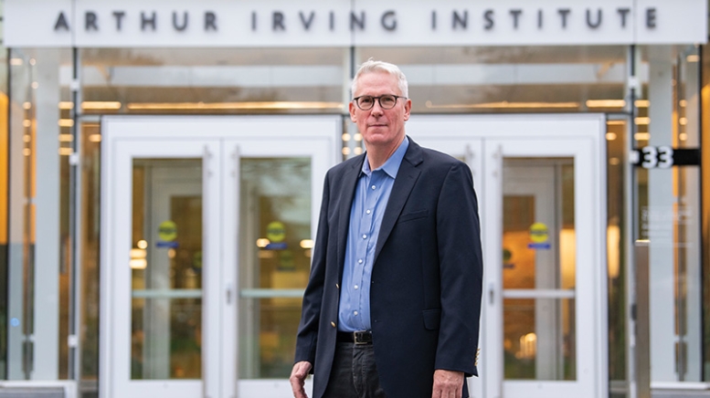 Man wearing suit, standing in front to building that says Arthur Irving Institute