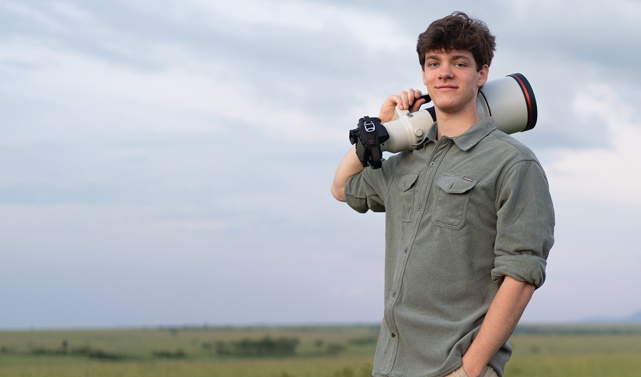 Man standing in field, holding large camera over shoulder