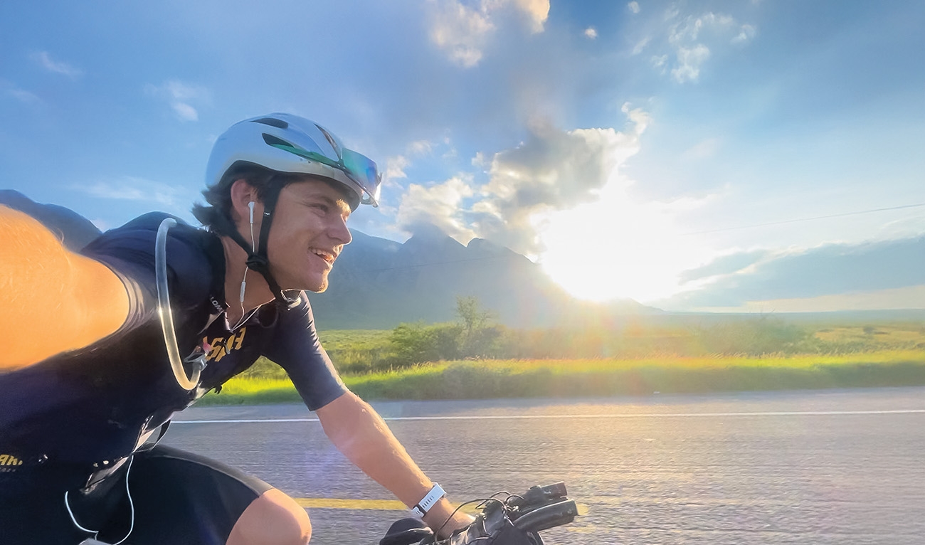 Man taking a selfie while riding bicycle on highway with mountains in background