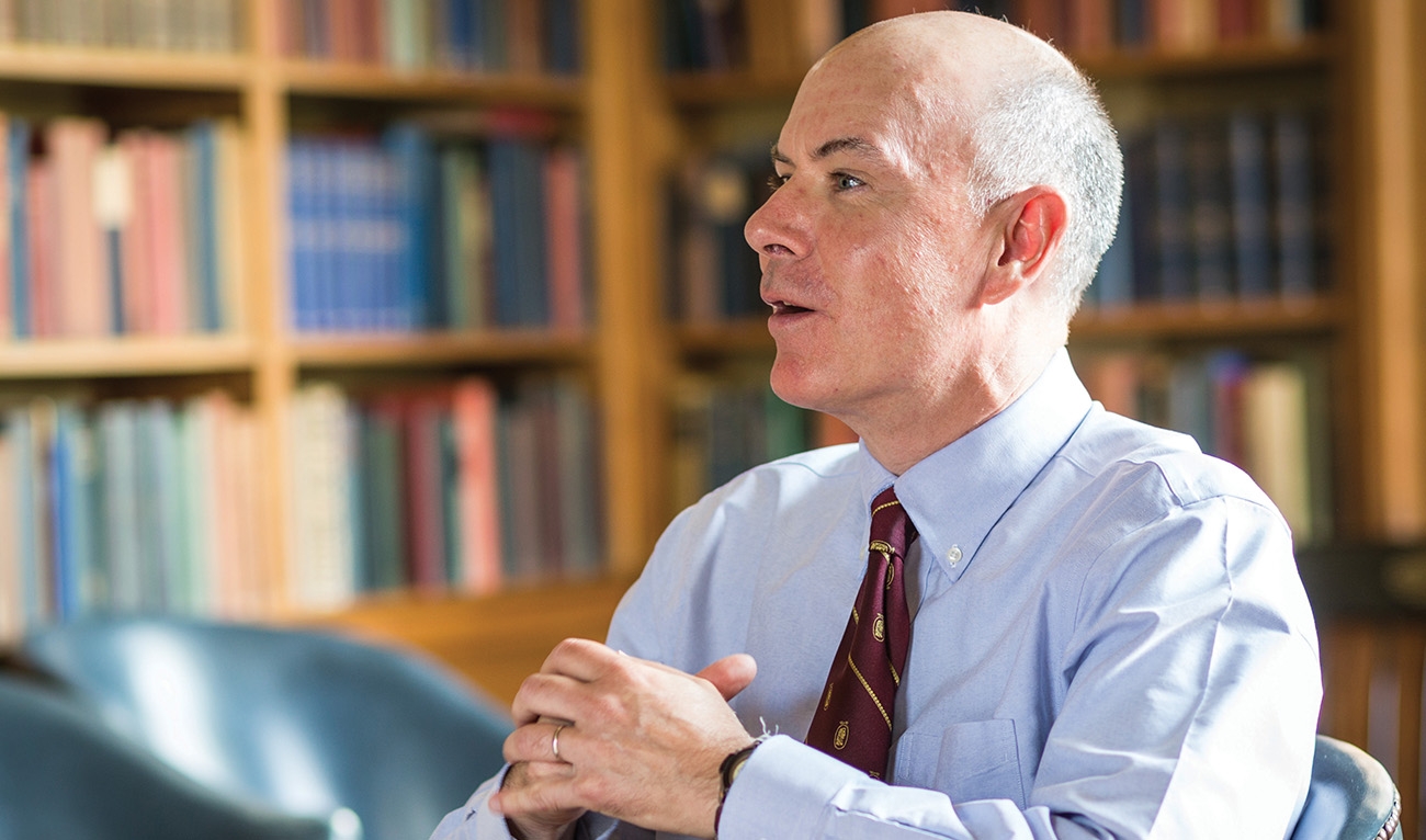 Man wearing a suit, bookshelves in background