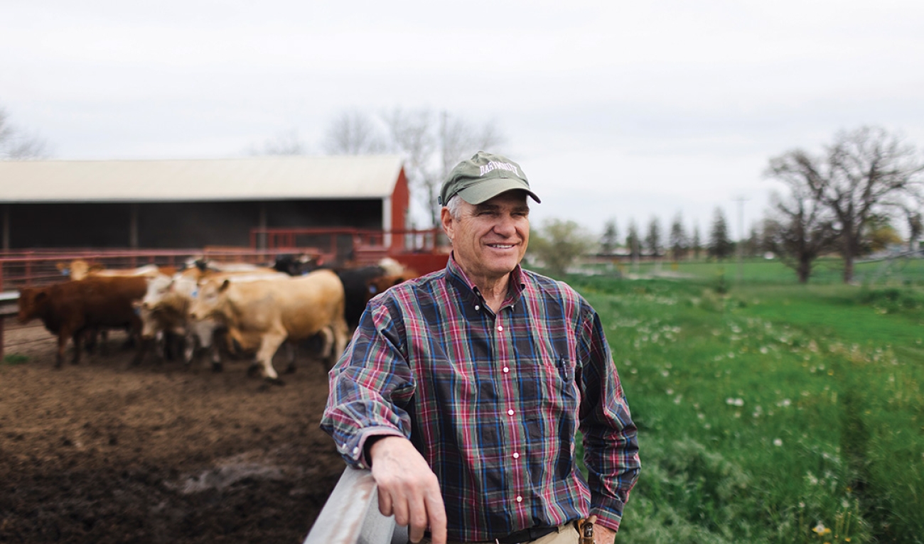 Man wearing flannel, standing next to pen with cows