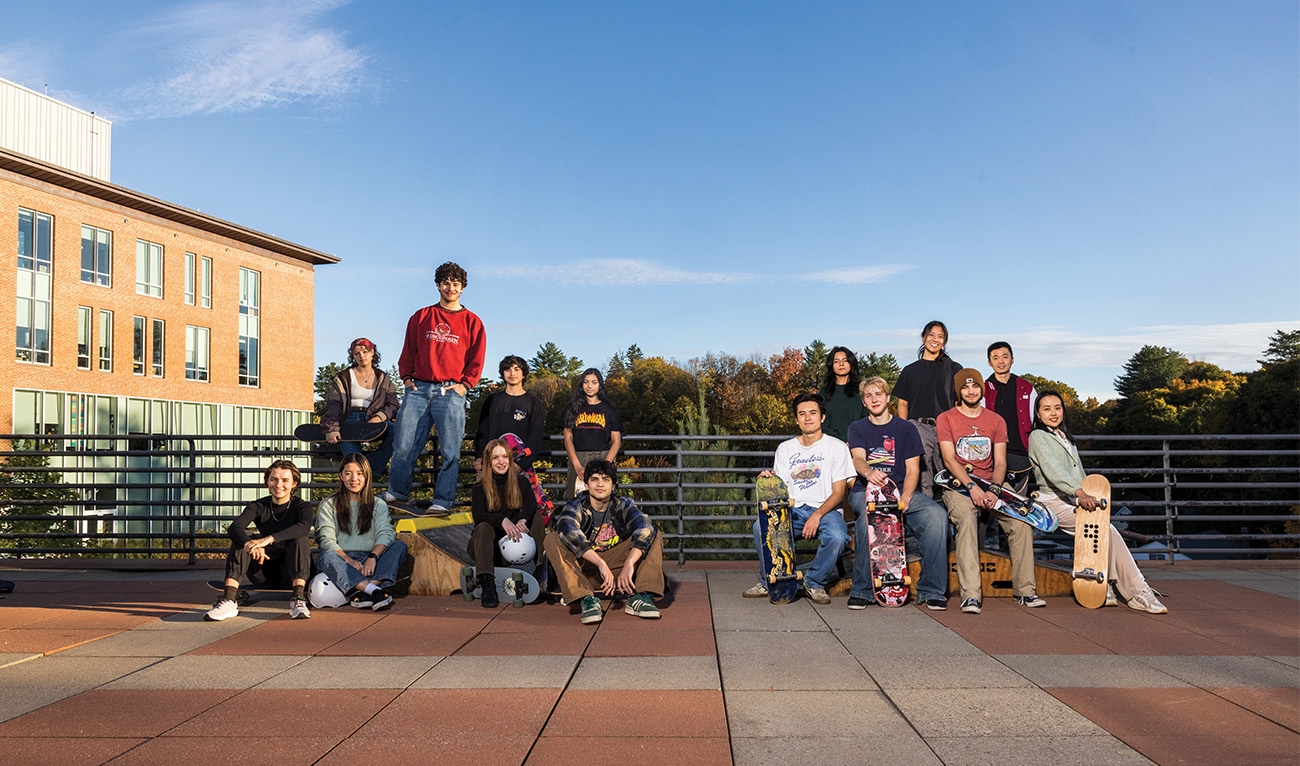 Two groups of students posing with skateboards and helmets on campus