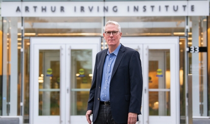 Man wearing suit, standing in front to building that says Arthur Irving Institute